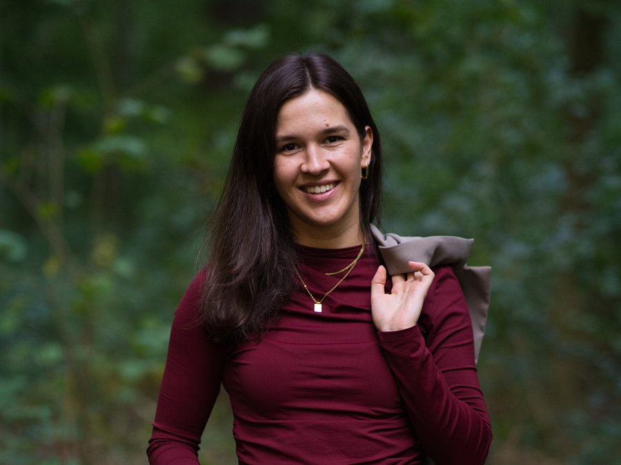 Leonie läuft lächelnd durch den Wald, den Blazer über der Schulter