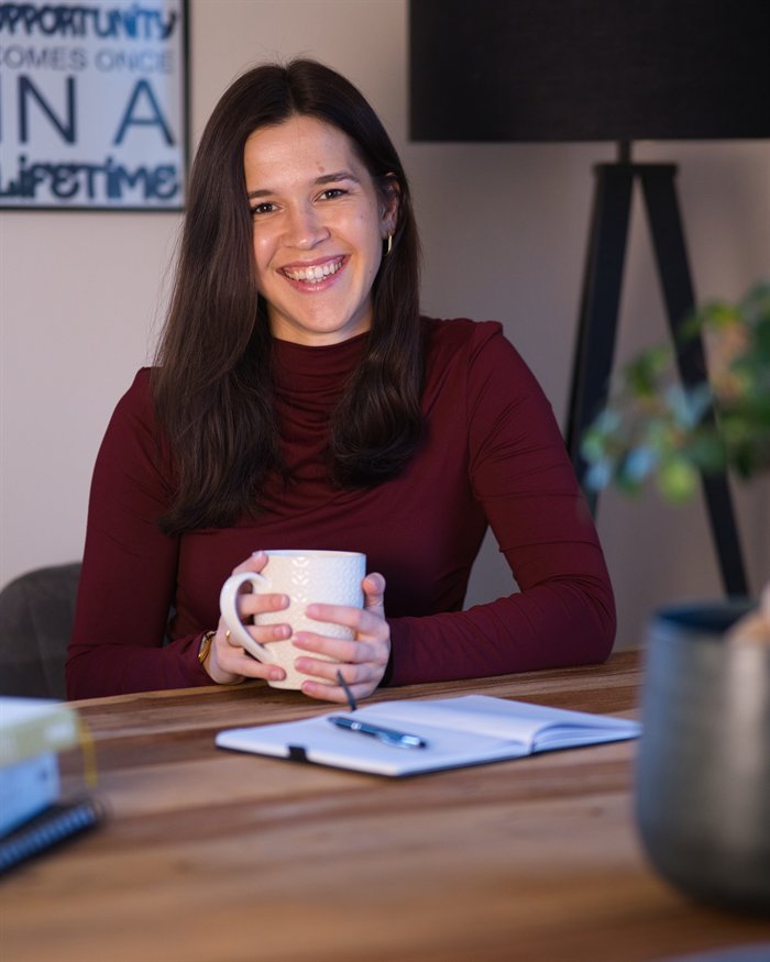 Leonie lächelt am Tisch und hält eine Tasse in den Händen